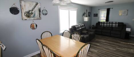 A dining area with a wooden table and chairs, a gray couch, and a plaid blanket.