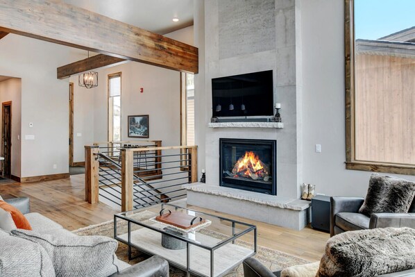 Amplia sala de estar con chimenea, una escalera y un ventanal grande.