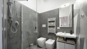 A modern bathroom with a glass-enclosed shower, a bidet, a sink with a mirror, and a towel rack. - EasyStayRome | Vatican Home | Near Metro (Roma)