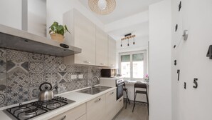 A modern kitchen with a gas stove, oven, and a microwave. There is a potted plant on the counter and a hanging light fixture above the sink. - EasyStayRome | Vatican Home | Near Metro (Roma)