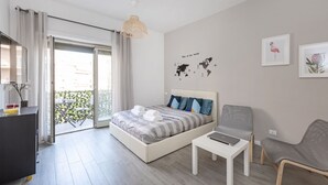 A modern bedroom with a bed, a desk, and a chair. There is a balcony with a view of the city. - EasyStayRome | Vatican Home | Near Metro (Roma)