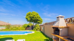 Un jardin avec une piscine, un barbecue et une pelouse agrémentée de chaises longues.
