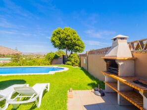 Ein Garten mit Swimmingpool, Grill und einer Rasenfläche mit Liegestühlen.