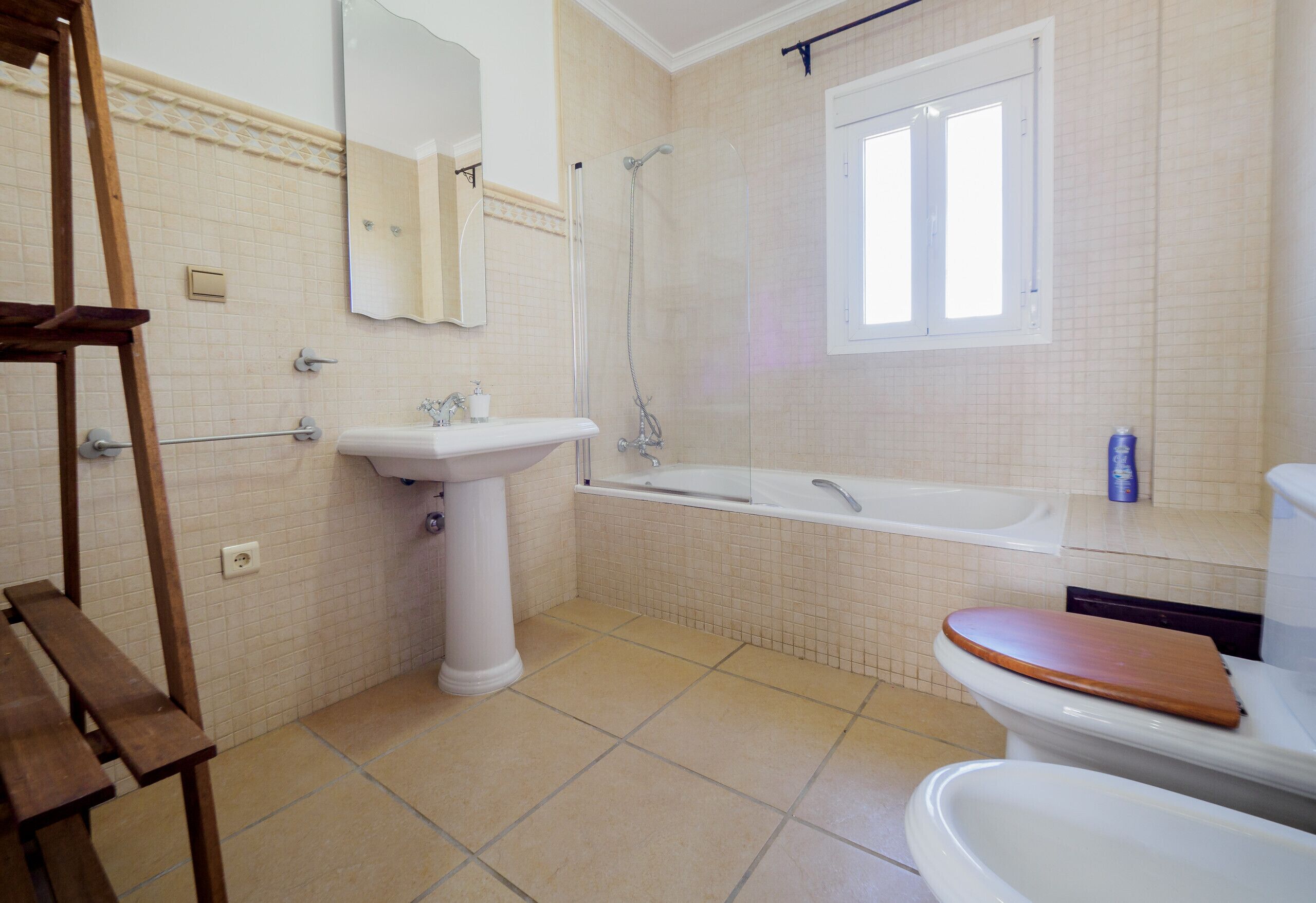 Un bagno con lavandino, WC, vasca e una panca in legno.