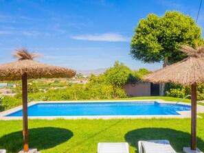 A swimming pool with two thatched umbrellas, surrounded by green grass and trees. - Cubo’s Villa Plumaria de Alhaurin / private pool / free wifi (Alhaurin de la Torre)