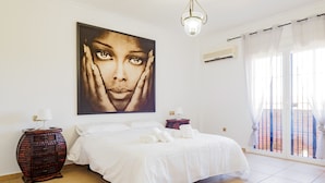Une chambre avec un grand lit, un climatiseur fixé au mur, un luminaire au plafond et une fenêtre avec des rideaux.