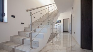 A modern staircase with marble steps and stainless steel railings, leading to a hallway with a dark wooden door and a painting on the wall. - Villa Tiara with Pool (Premantura)