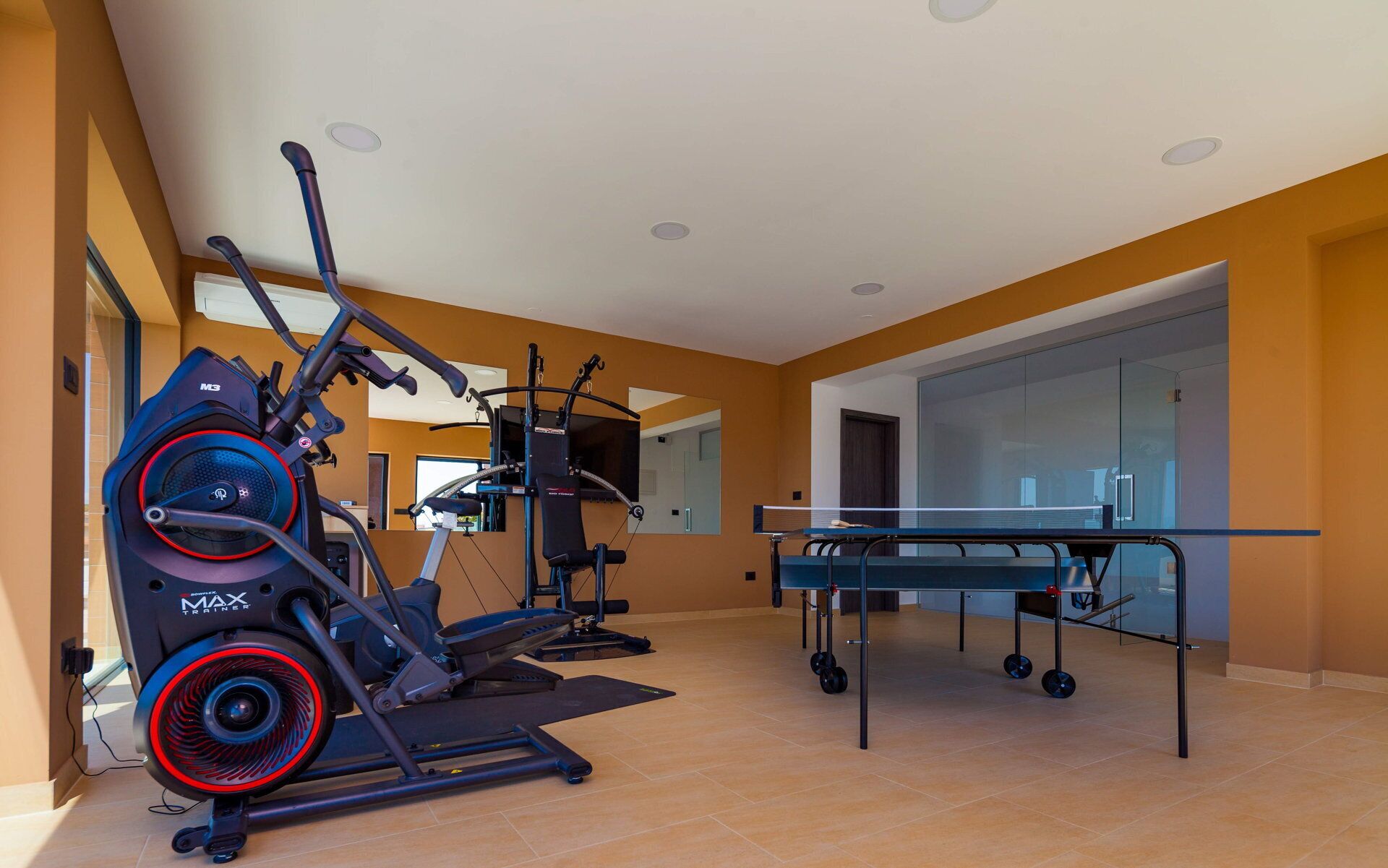 Un gimnasio en casa con equipo de cardio, una mesa de ping pong y un espejo grande.