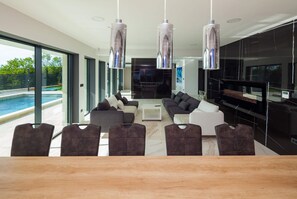 A modern living room with a pool, grey sofas, and a wooden dining table.