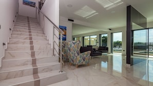 A modern interior with a marble staircase, a patterned armchair, a dark sofa, and a glass-enclosed balcony with a view. - Villa Siena with Pool (Premantura)