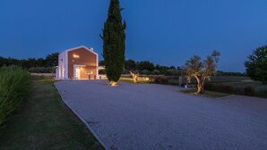 Une maison moderne avec une allée en gravier, un grand cyprès et un jardin bien entretenu.