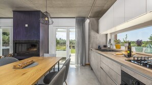 Une cuisine moderne dotée d’un four encastré, un coin repas avec une table et des chaises en bois, et une vue sur l’extérieur grâce à de grandes fenêtres.
