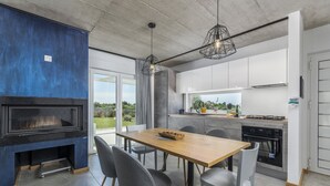 Une cuisine moderne dotée d’une cuisinière intégrée, d’un coin repas avec une table en bois et des chaises grises, et d’une grande fenêtre offrant une vue sur l’extérieur.