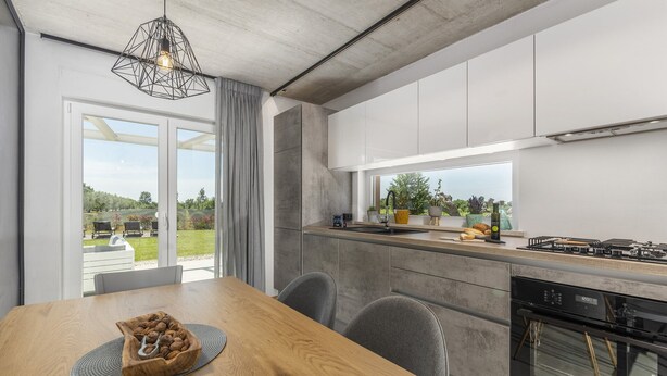 Une cuisine moderne dotée d’une grande fenêtre, d’une table à manger avec des chaises et d’un four encastré.