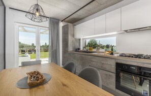 Una cuina moderna amb un finestral gran, una taula de dinar amb cadires i un forn encastrat.