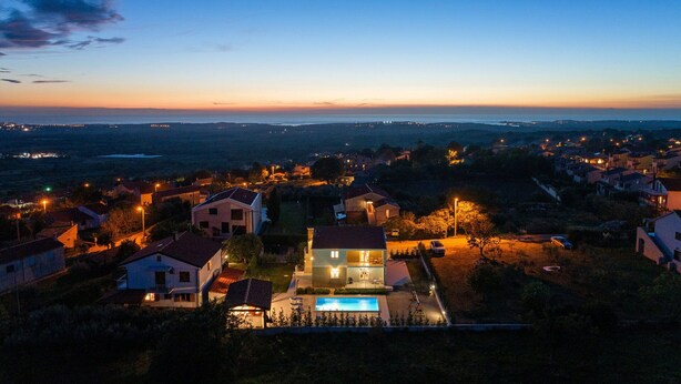 A residential area with houses, a swimming pool, and a view of the sea at dusk. - Villa Comfort with Pool (Kaštelir)