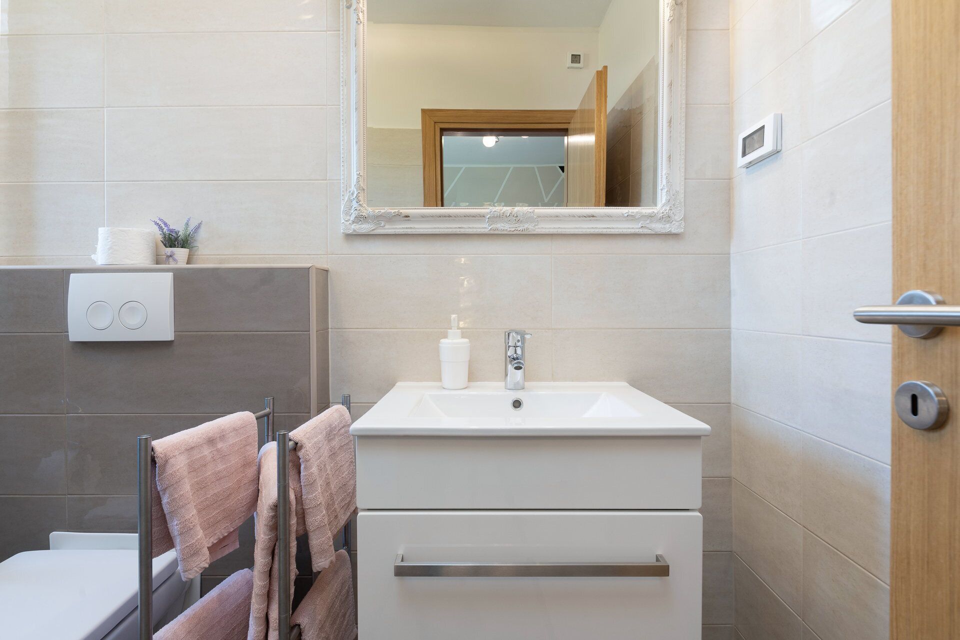 Un bany amb un lavabo blanc, un mirall, un escurapulides amb tovalloles, un vàter i una zona de dutxa.