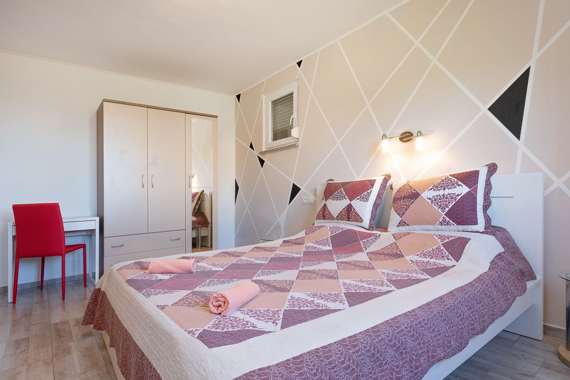 A bedroom with a bed, a red chair, a wardrobe, and a desk.