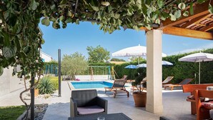 A poolside area with wicker furniture, umbrellas, and a swing set. - Villa Comfort with Pool (Kaštelir)