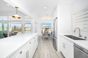 A modern kitchen with white cabinetry, a large island, and a view of the beach.