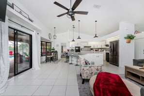 Relax in this stylish living space with a central kitchen island, sofa, and sliding glass door to an outdoor area with a pool.