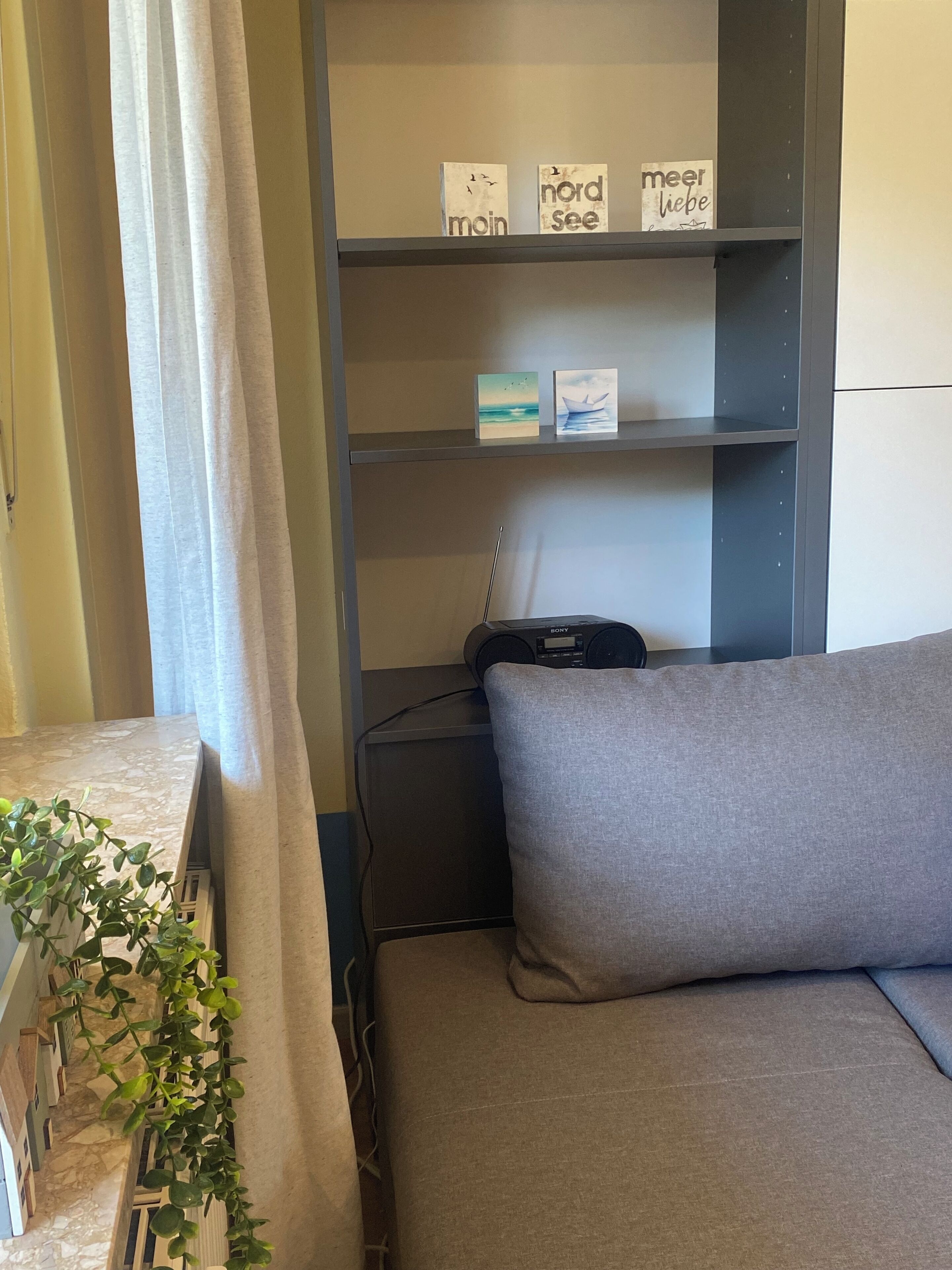A room with a grey sofa, a bookshelf with decorative items, and a Sony speaker.