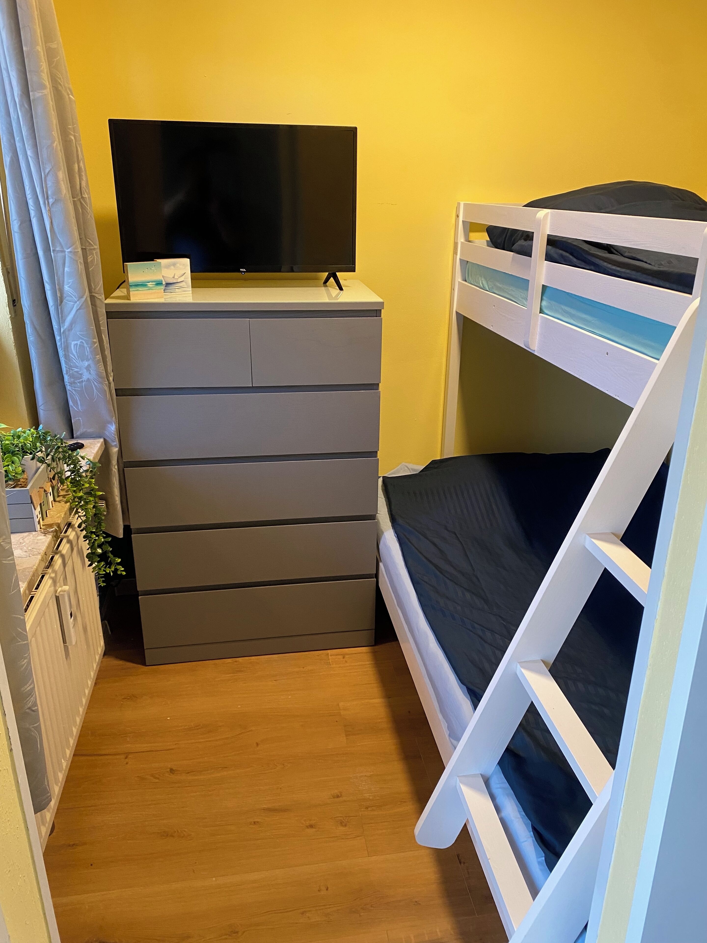 Ein kleines Zimmer mit einem Etagenbett, einer Kommode und einem Flachbildfernseher sowie einer kleinen Pflanze.