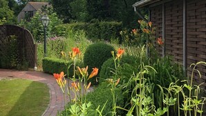Un jardin agrémenté d’un bâtiment en briques, d’un chemin pavé et de diverses plantes et fleurs.