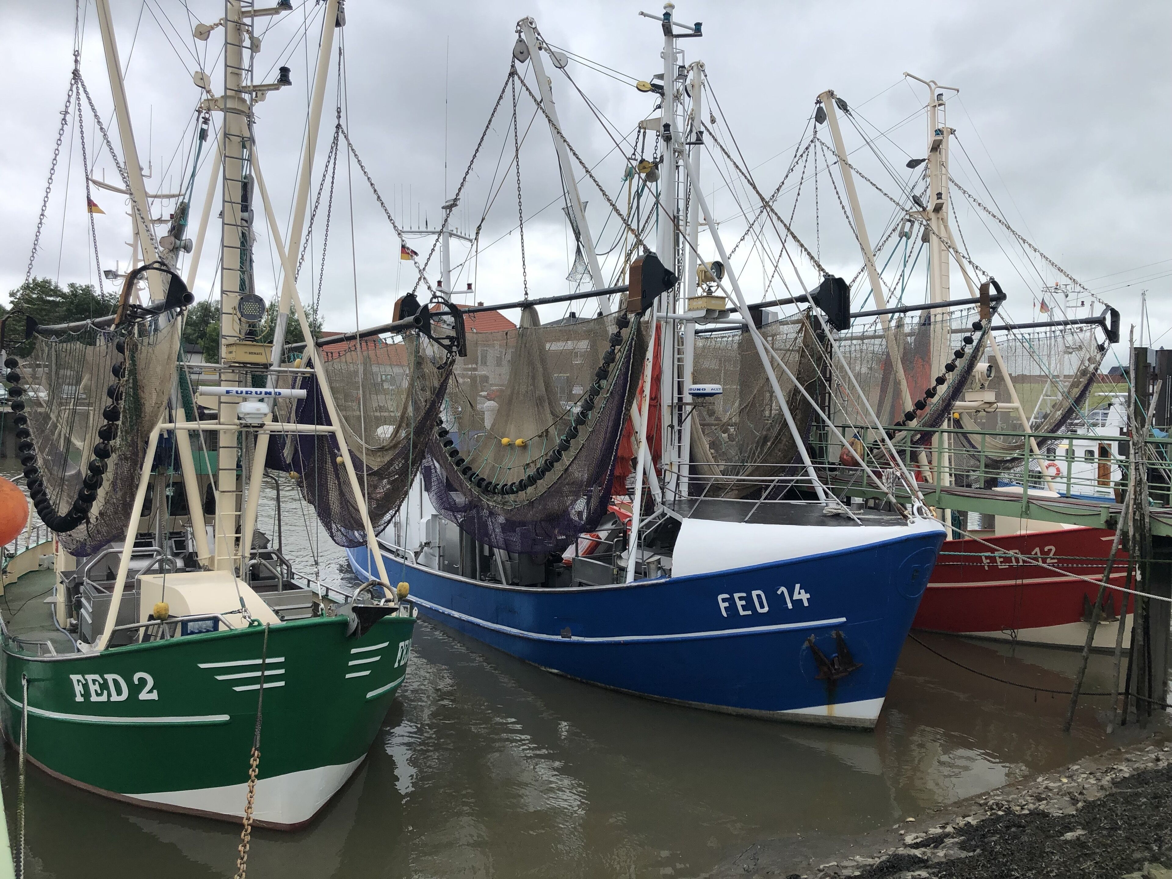 Several fishing boats docked at a harbor with nets and equipment visible.