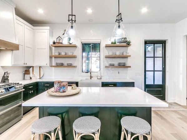A modern kitchen with a central island, wooden shelves, and pendant lighting.