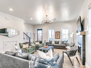 A spacious living room with a fireplace, a staircase, and large windows.