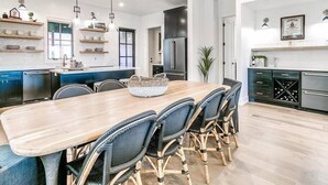 A modern kitchen with a wooden dining table, wicker chairs, built-in cabinets, and pendant lighting. - Luxury Carlton Landing Home Golf Cart Included! (Carlton Landing)