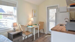 A compact kitchen with a dining area, a built-in oven, and a window with blinds. - Cozy Colorful Cottage Perfect for 2! (Eastham)