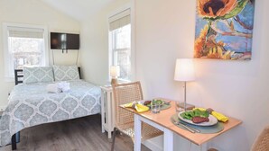 Une chambre avec un lit, une table à manger avec une assiette de nourriture, et un tableau accroché au mur.