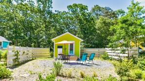 Un petit bâtiment d’un seul étage, à l’extérieur d’un vert vif et doté d’une porte blanche, entouré d’une clôture en bois et d’une terrasse en gravier avec deux chaises bleues et une table.