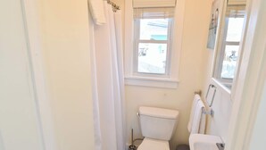 Une petite salle de bain blanche, avec des toilettes, un lavabo et une fenêtre.
