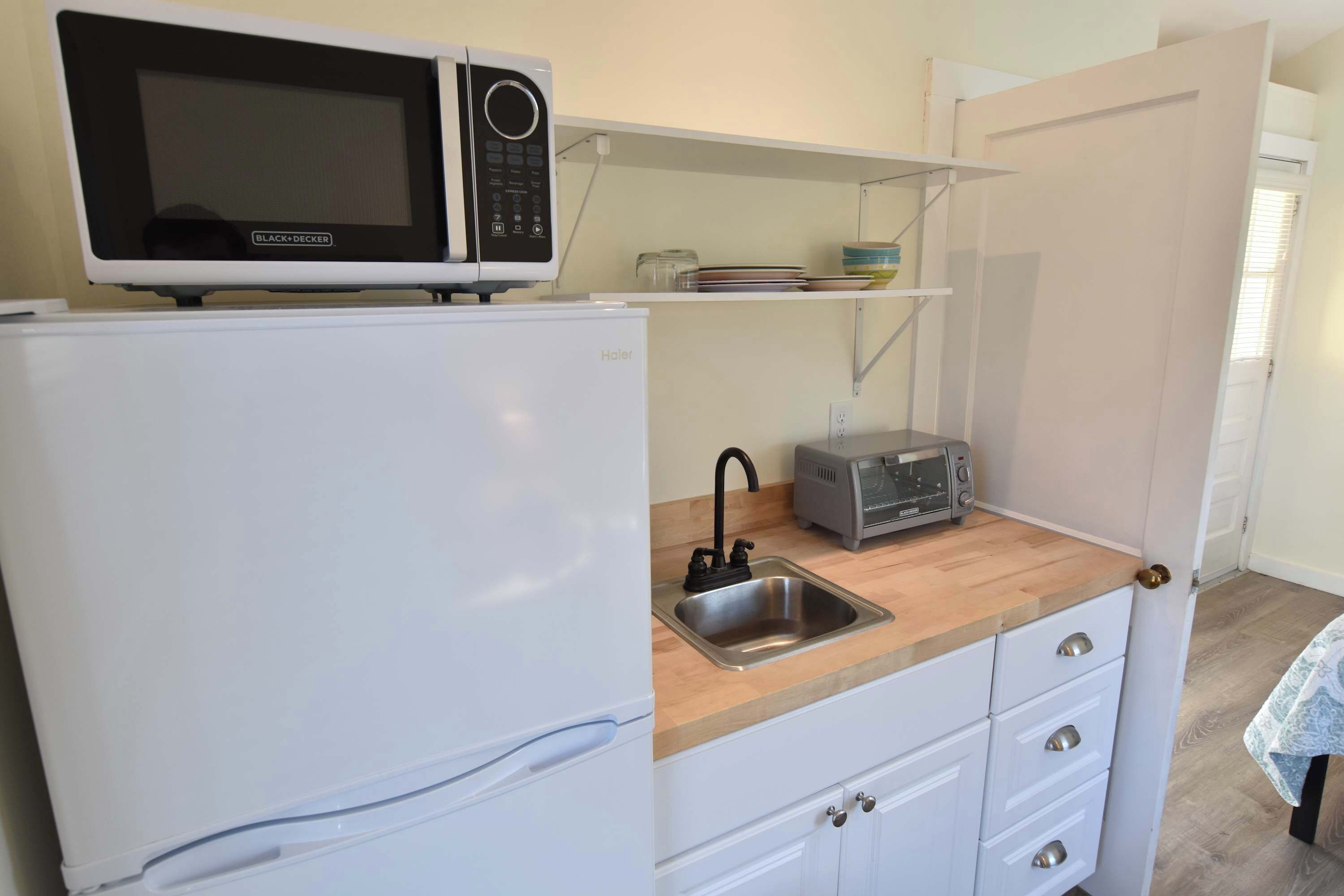 A compact kitchenette with a white refrigerator, a microwave, a toaster, and a sink.