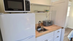 A compact kitchenette with a white refrigerator, a microwave, a toaster, and a sink. - Dreamy Cottage for Two! Close to Beaches! (Eastham)