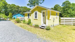 A yellow mobile home with a porch, a blue house in the background, and a gravel driveway. - Bright Cottage Close to Bayside Beaches! (Eastham)
