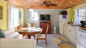 A cozy kitchen with wooden ceiling, a dining area with a round table and chairs, and a built-in TV. - Bright Cottage Close to Bayside Beaches! (Eastham)