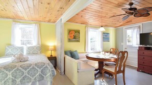 A room with a bed, a sofa, a dining table with chairs, a TV, and a ceiling fan. - Bright Cottage Close to Bayside Beaches! (Eastham)