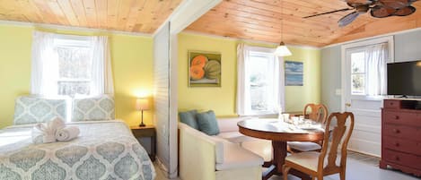 A room with a bed, a sofa, a dining table with chairs, a TV, and a ceiling fan.
