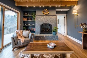 A modern living room with a fireplace, wooden furniture, and a bookshelf. - The Forest Glade House (Front Royal)