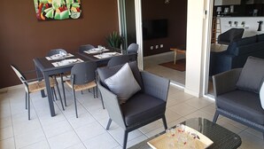 A dining area with a table set for four, surrounded by wicker chairs with cushions. - 3-BEDROOM APARTMENT IN LUXURY RESIDENCE WITH SEA VIEW (Les Trois-Îlets)