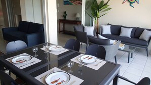 A dining area with a glass table set for four, surrounded by dark-colored furniture. - 3-BEDROOM APARTMENT IN LUXURY RESIDENCE WITH SEA VIEW (Les Trois-Îlets)