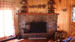 A cozy room with a stone fireplace, wooden shelves, and a plaid curtain. - RMNP,Longs Peak Views,Fireplace,Grill,Deck,Mtn Neighborhood Above Estes Park (Estes Park)