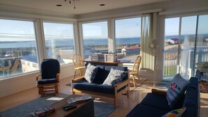 A spacious living room with a large window offering a view of the sea and a rocky shoreline. There are two sofas, a wooden coffee table, and a small side table. - Waterfront Acadian Home on Mavillette Beach at Cape St. Marys (Church Point)