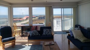 A spacious living room with a large window, a ceiling fan, and a view of the sea. - Waterfront Acadian Home on Mavillette Beach at Cape St. Marys (Church Point)