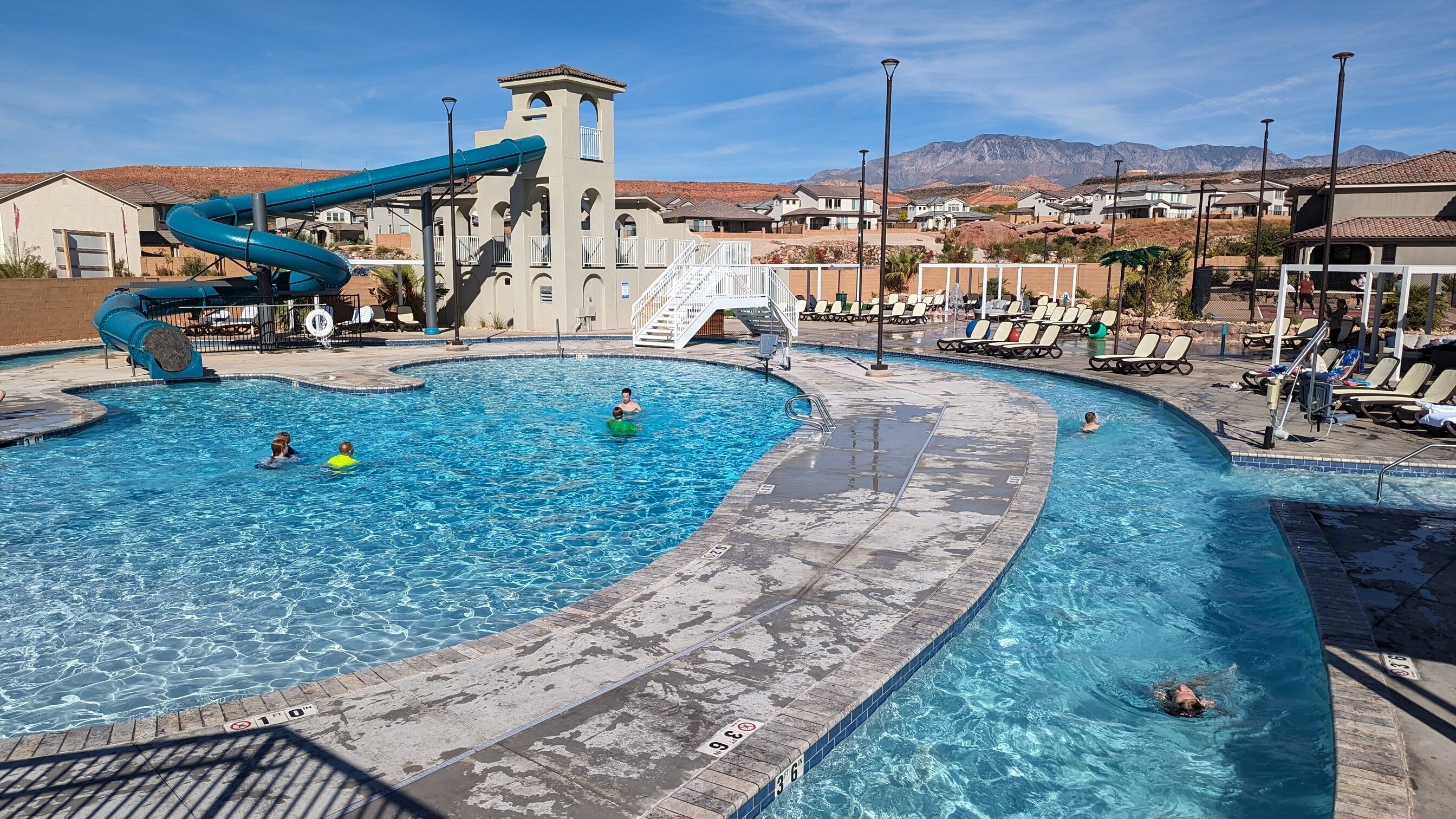 A swimming pool with a water slide, lounge chairs, and a mountain view in the background.