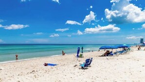 Ein Strand mit blauem Himmel, sandigem Ufer und vereinzelten Sonnenschirmen und Stühlen.